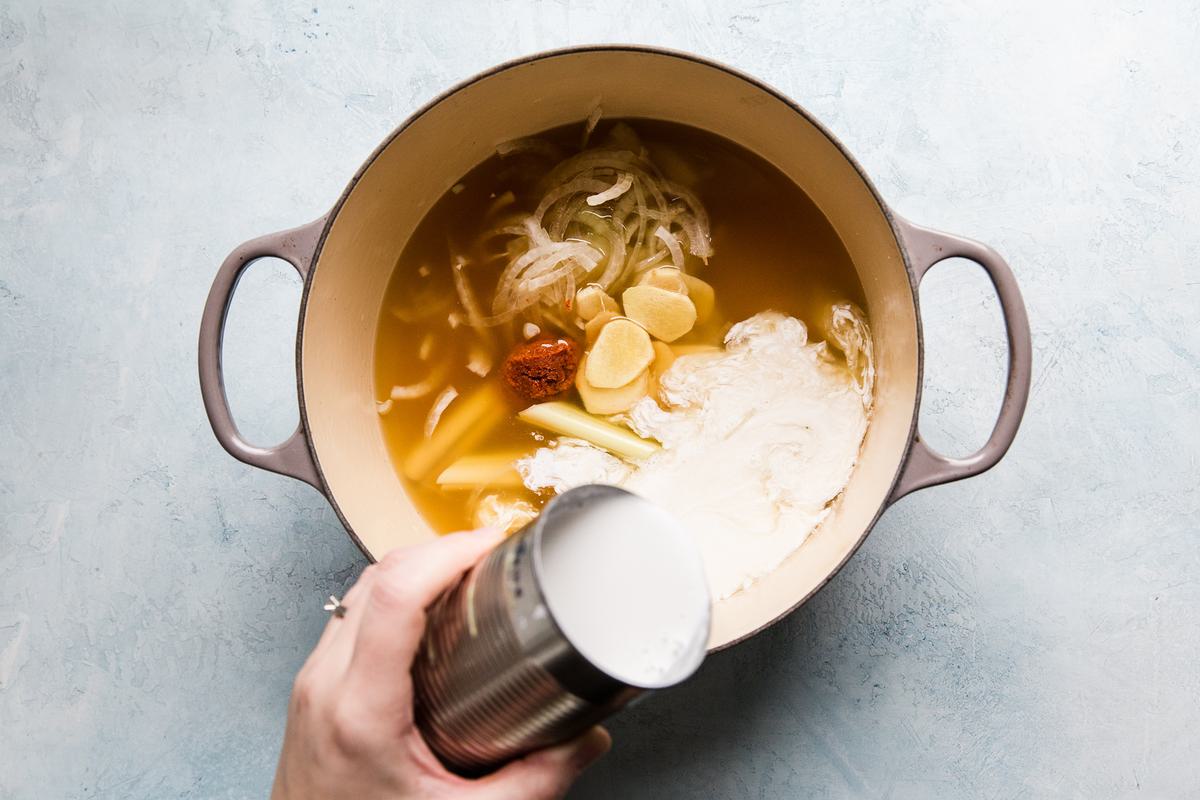Chicken stock, coconut broth, lemon grass, red thai curry and ginger in a soup pot.