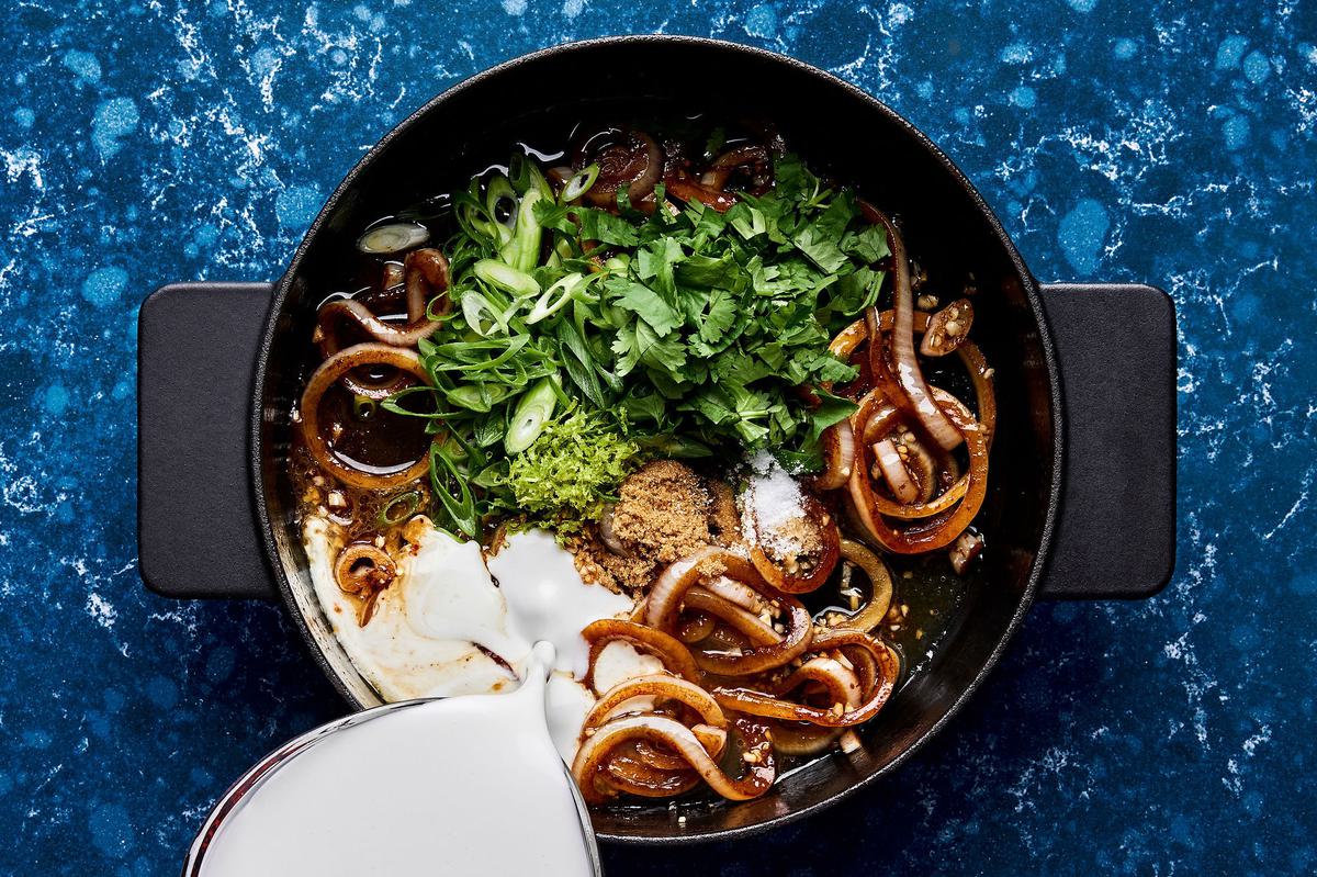coconut milk being poured into a skillet with cilantro, lime zest, lime juice, green onions, salt, and brown sugar
