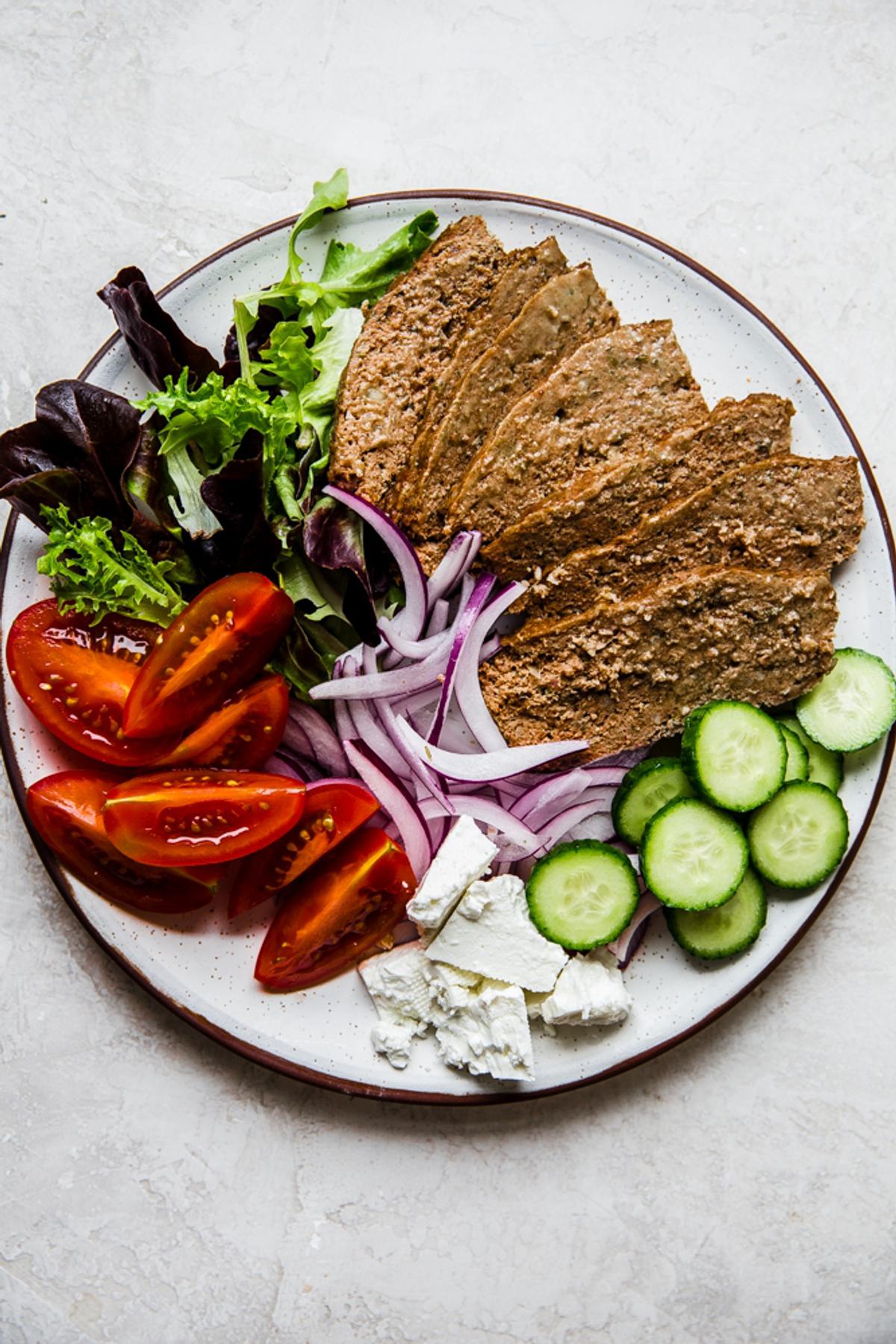 Homemade gyro meat sliced on a platter with cucumbers, feta, tomatoes, onions